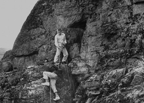 Two men conquering difficulties while climbing up a rocky cliff, displaying manvotional determination.